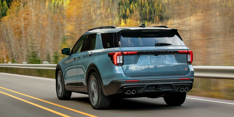 Rear exterior view of a 2026 Ford Explorer driving on a highway, showcasing LED taillights, sporty rear design, and modern SUV styling.