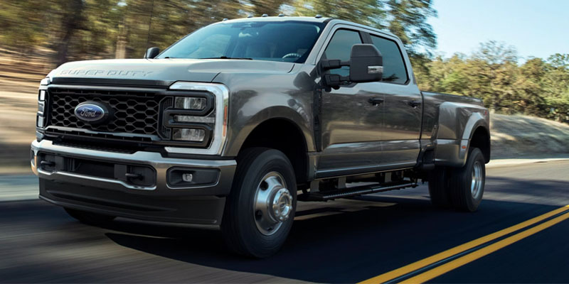 2026 Ford F-250 Super Duty driving on a road, featuring a bold front grille, crew cab configuration, and heavy-duty dual rear wheels.